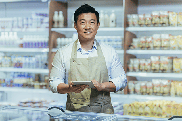 Homme asiatique souriant face à la caméra, tenant une tablette, debout dans une vitrine.