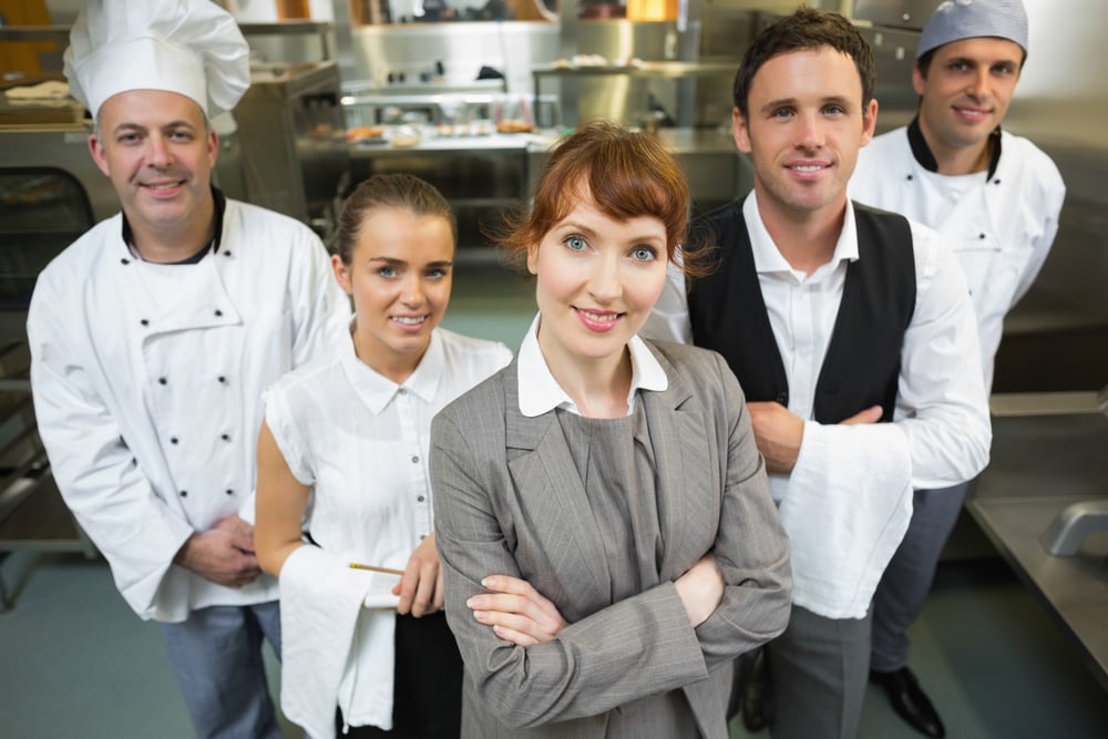 Mignonne femme manager posant avec le personnel dans une cuisine moderne