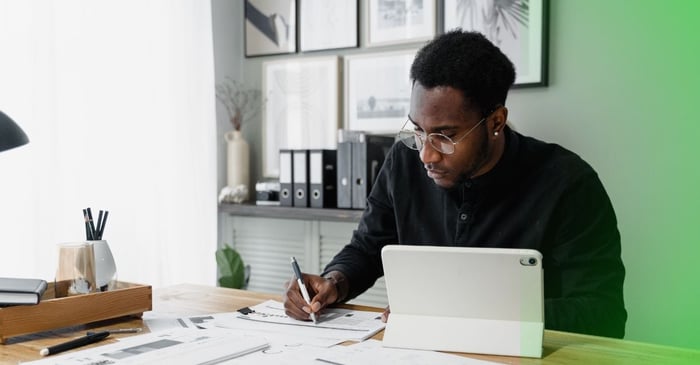 Homme assis à un bureau avec un iPad prenant des notes sur des documents