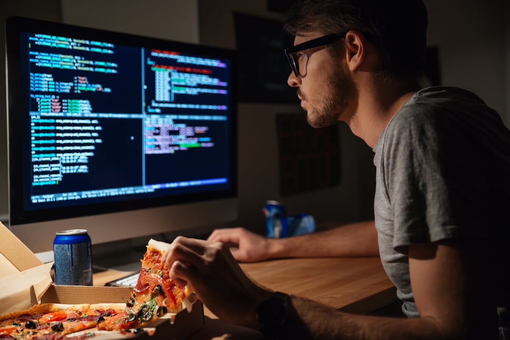 Profil d'un jeune développeur de logiciels concentré, mangeant des pizzas et codant à la maison