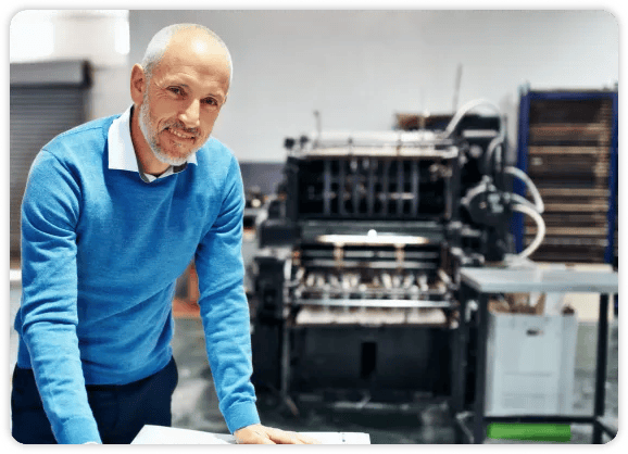 homme âgé en chemise bleue debout devant une machine à plier le papier