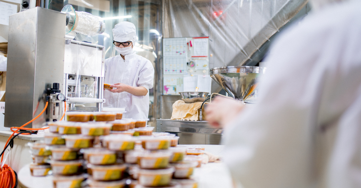 Personne en blouse de laboratoire et masque posant des couvercles sur des emballages alimentaires derrière un monticule d'emballages